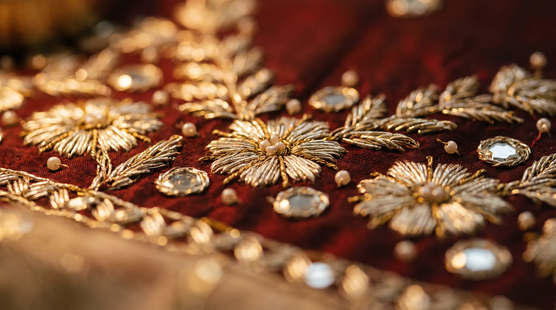 Gold zari embroidery on deep oxblood silk, lit by candlelight